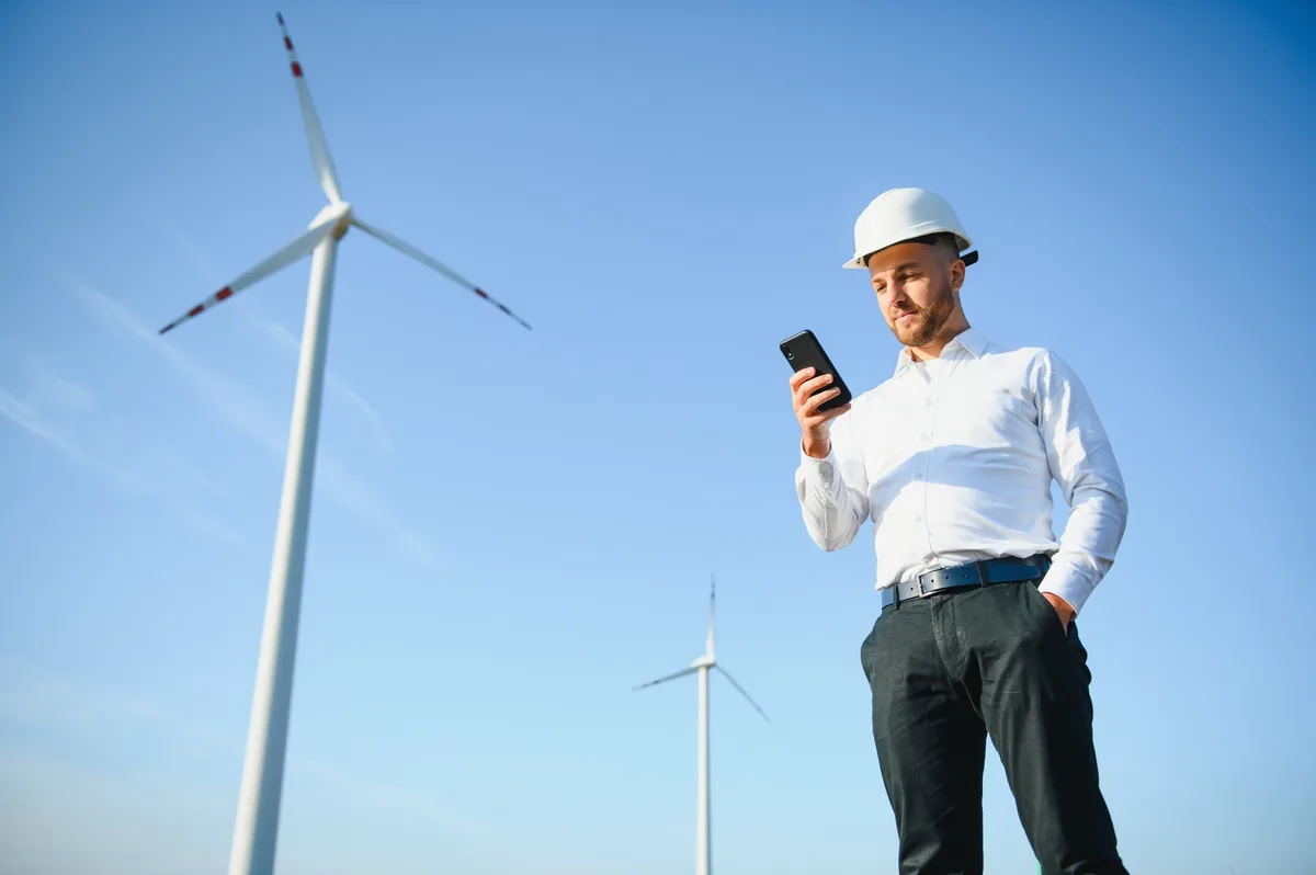 A field technician checking a work order on a mobile device near a wind turbine